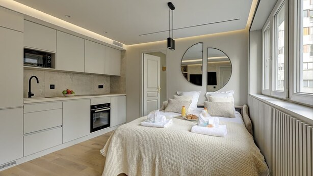 Une chambre moderne avec un grand lit, une cuisine intégrée équipée d’un four à micro-ondes et un grand miroir.