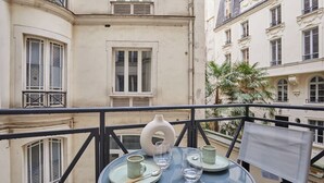 A balcony with a table set for two, a white vase, and a palm tree in the background.