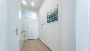 A hallway with a wooden floor, white walls, a door with a window, and a framed picture of a mountain landscape. - Cozy 1BR Apartment in Prime Location (Vienna)