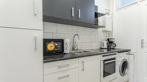 A modern kitchen with white cabinets, a built-in microwave, a coffee maker, a washing machine, and a sink. - Cozy 1BR Apartment in Prime Location (Vienna)
