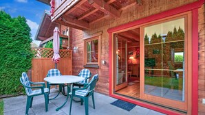 Una cabaña de madera con un patio que incluye una mesa, sillas, una puerta corrediza de vidrio y una valla de madera.
