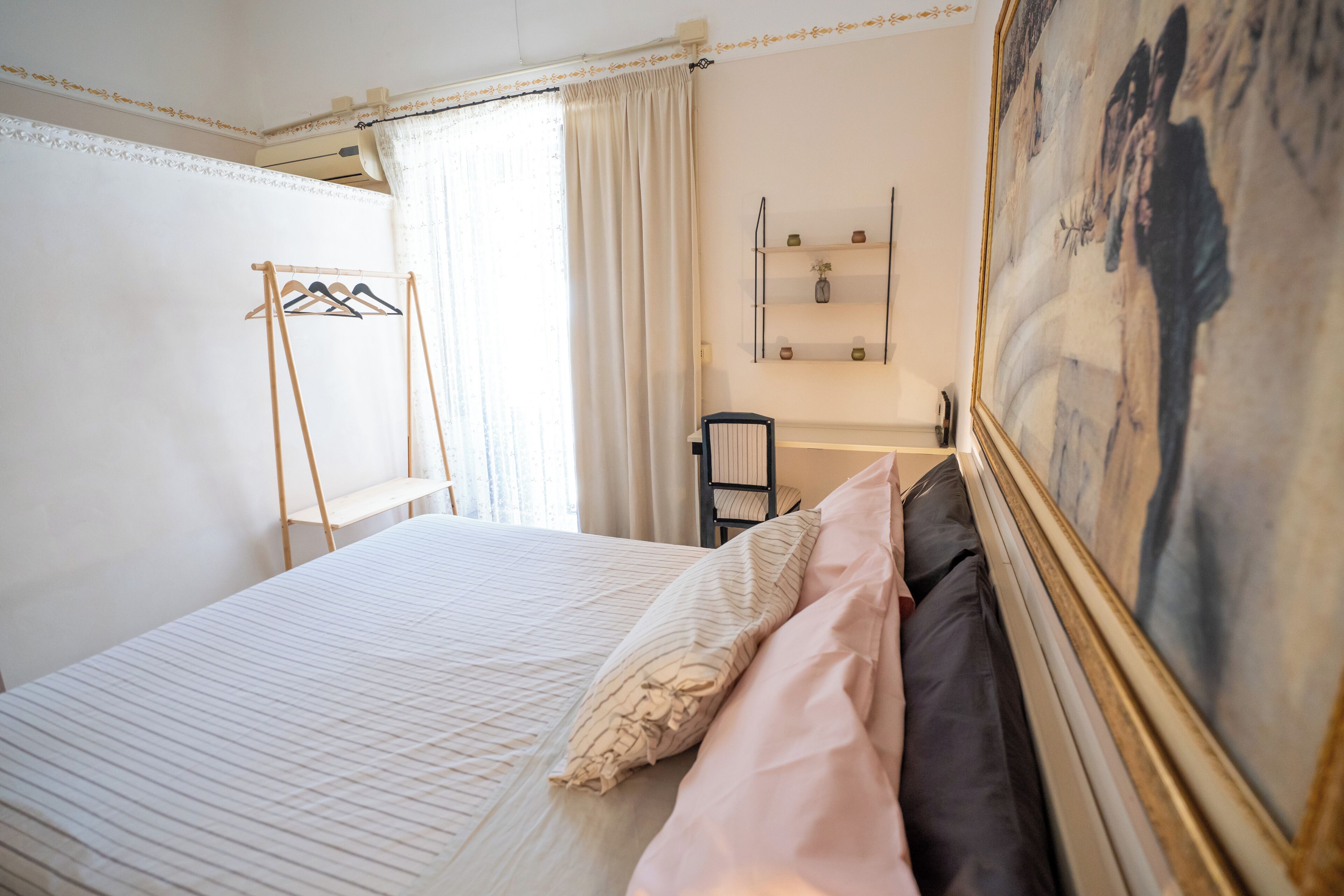 Un dormitorio ordenado con cama, una silla, un escritorio y un cuadro en la pared.