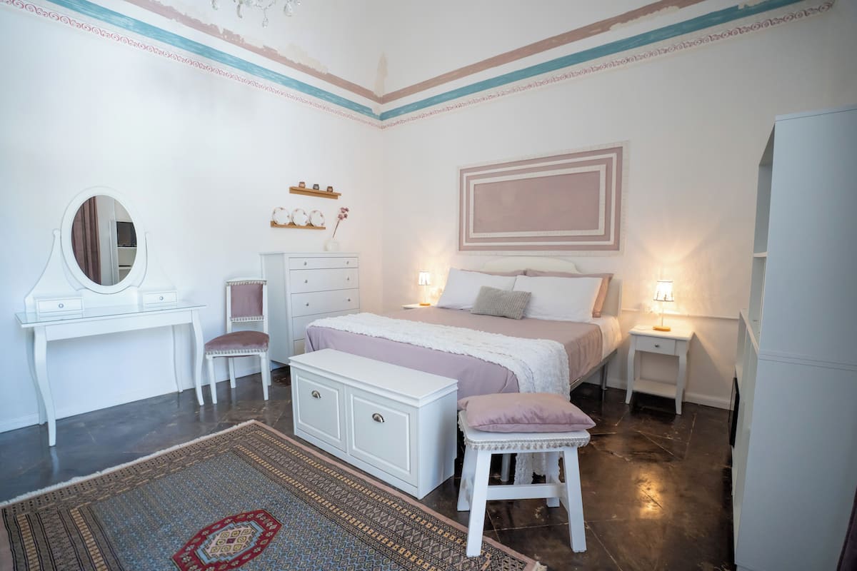 A bedroom with a bed, bedside tables, a dresser, a mirror, and a rug.