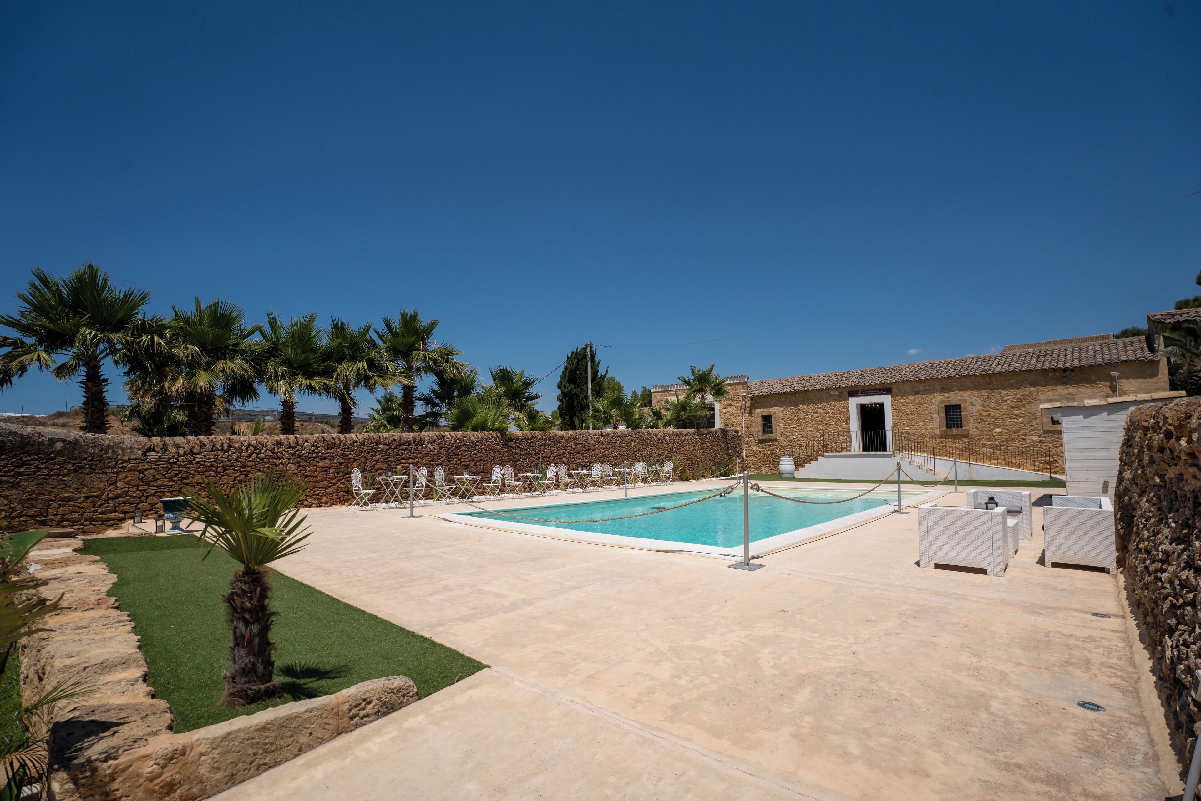 A pool area with a stone wall, palm trees, and outdoor seating.