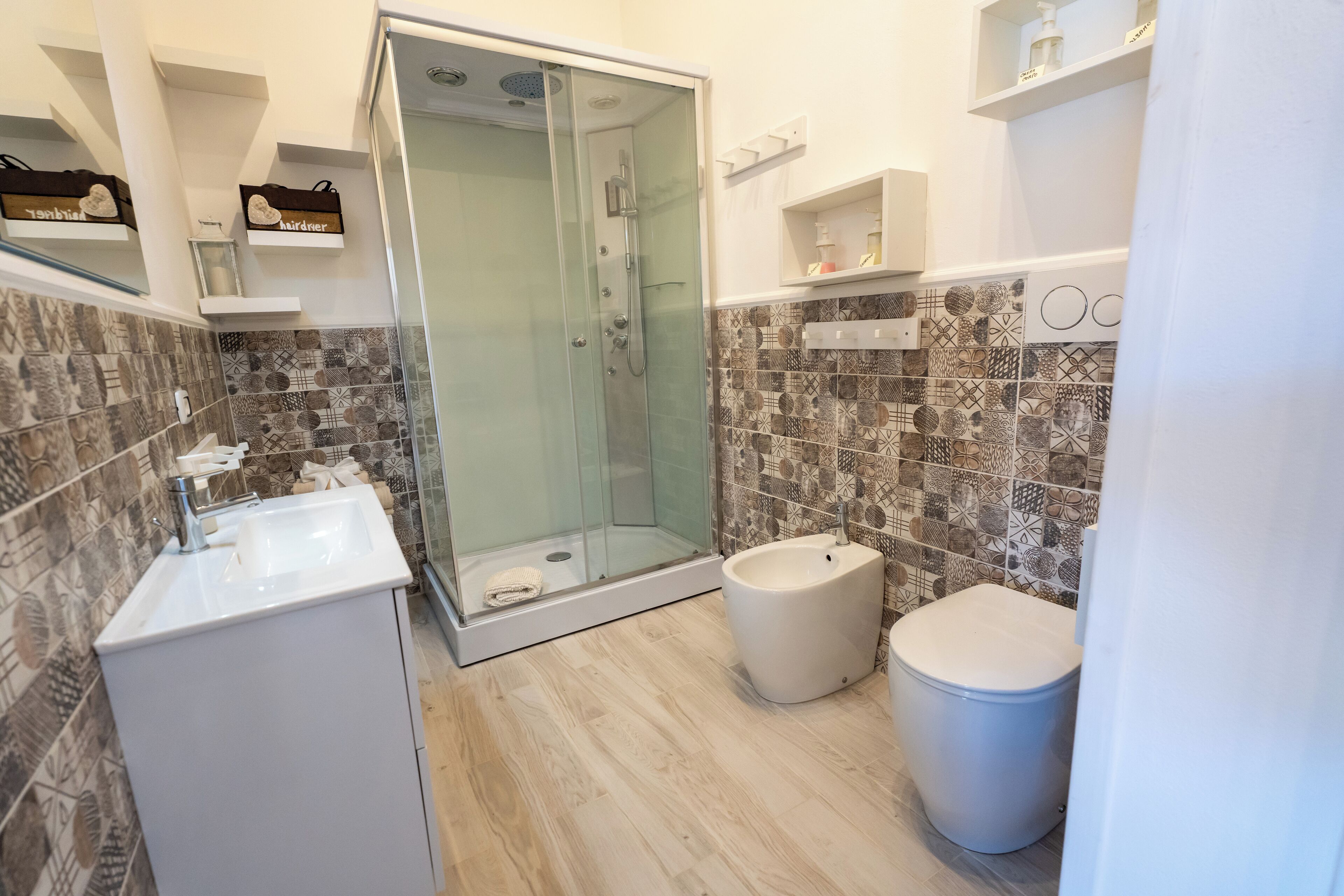Un baño moderno con ducha envuelta en vidrio, un lavabo blanco, un inodoro y baldosas con diseño.