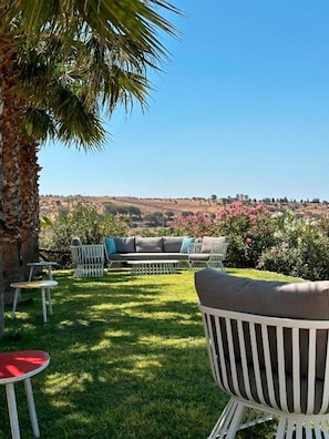 A patio with outdoor furniture, a palm tree, and a view of a hilly landscape. - Feudo Nobile (Gela)