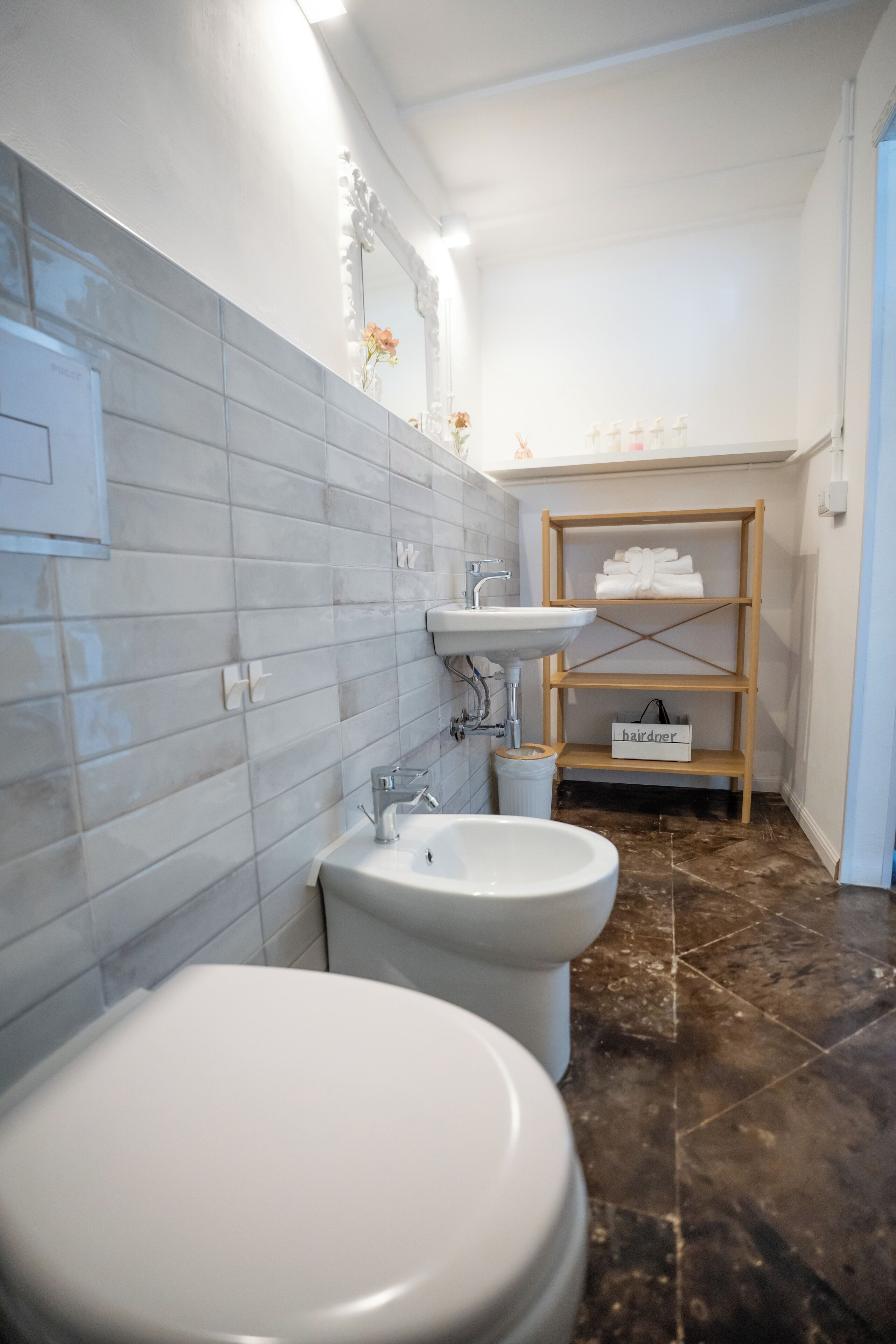 A bathroom with a white sink, a toilet, and a bidet. There is a shelf with towels and a sign that says "hairdresser".