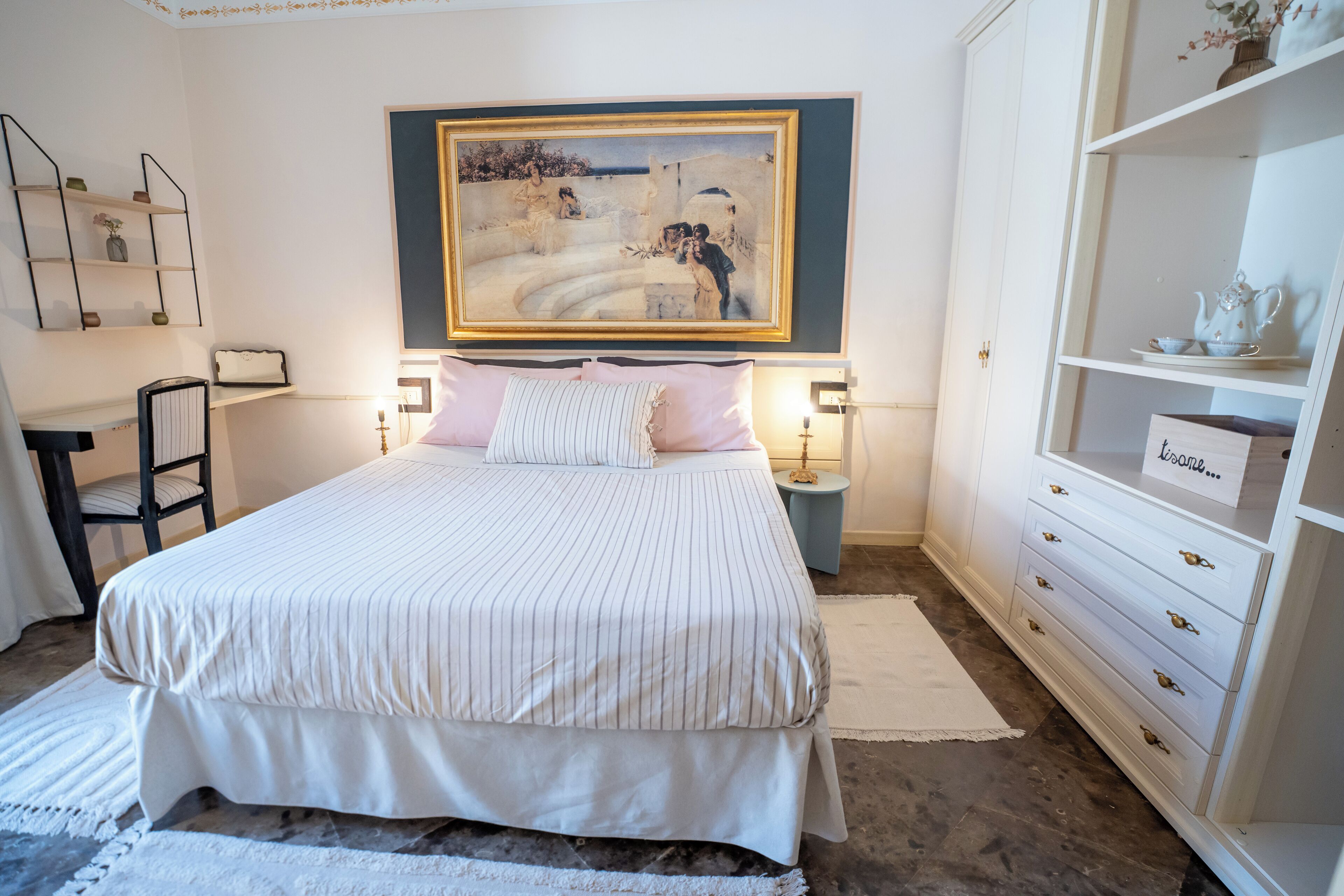 A neatly arranged bedroom with a large bed, bedside tables, a dresser, and a painting above the bed.