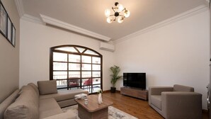 Un salon comprenant un canapé, deux fauteuils, une table basse, un téléviseur et une grande fenêtre donnant sur l’extérieur.