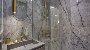 A modern bathroom with a marble wall, a gold faucet, and a glass-enclosed shower.