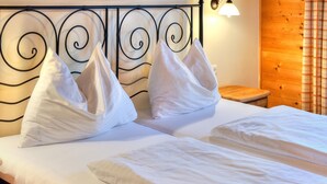 A double bed with white linens and decorative pillows, a bedside table, and a wall-mounted light fixture.
