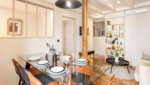 A dining area with a glass table, wooden chairs, and a modern pendant light. - Superb Ac apartment in the heart of the Marais (Paris)