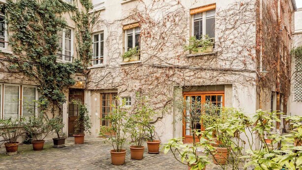 A courtyard with potted plants, a wooden door, and a building with ivy-covered walls. - Superb Ac apartment in the heart of the Marais (Paris)