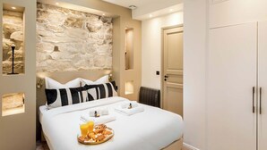 A hotel room with a stone wall, a bed with white bedding, a breakfast tray, and a wardrobe. - Superb Ac apartment in the heart of the Marais (Paris)