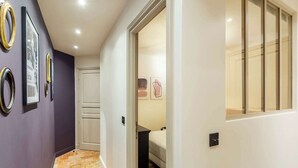A hallway with a purple wall, a tiled floor, and a door leading to a bedroom with a bed and artwork. - Superb Ac apartment in the heart of the Marais (Paris)