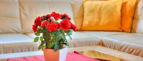 Un canapé blanc avec des coussins jaunes, une table basse en verre avec un set de table rouge et une plante en pot ornée de fleurs rouges.