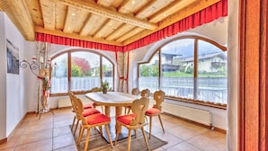 Ein Essbereich mit Holztisch und -stühlen, großen Fenstern mit Vorhängen und Blick auf Häuser und Berge.