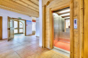An interior corridor with wooden paneling, a tiled floor, and a visible elevator with a control panel.