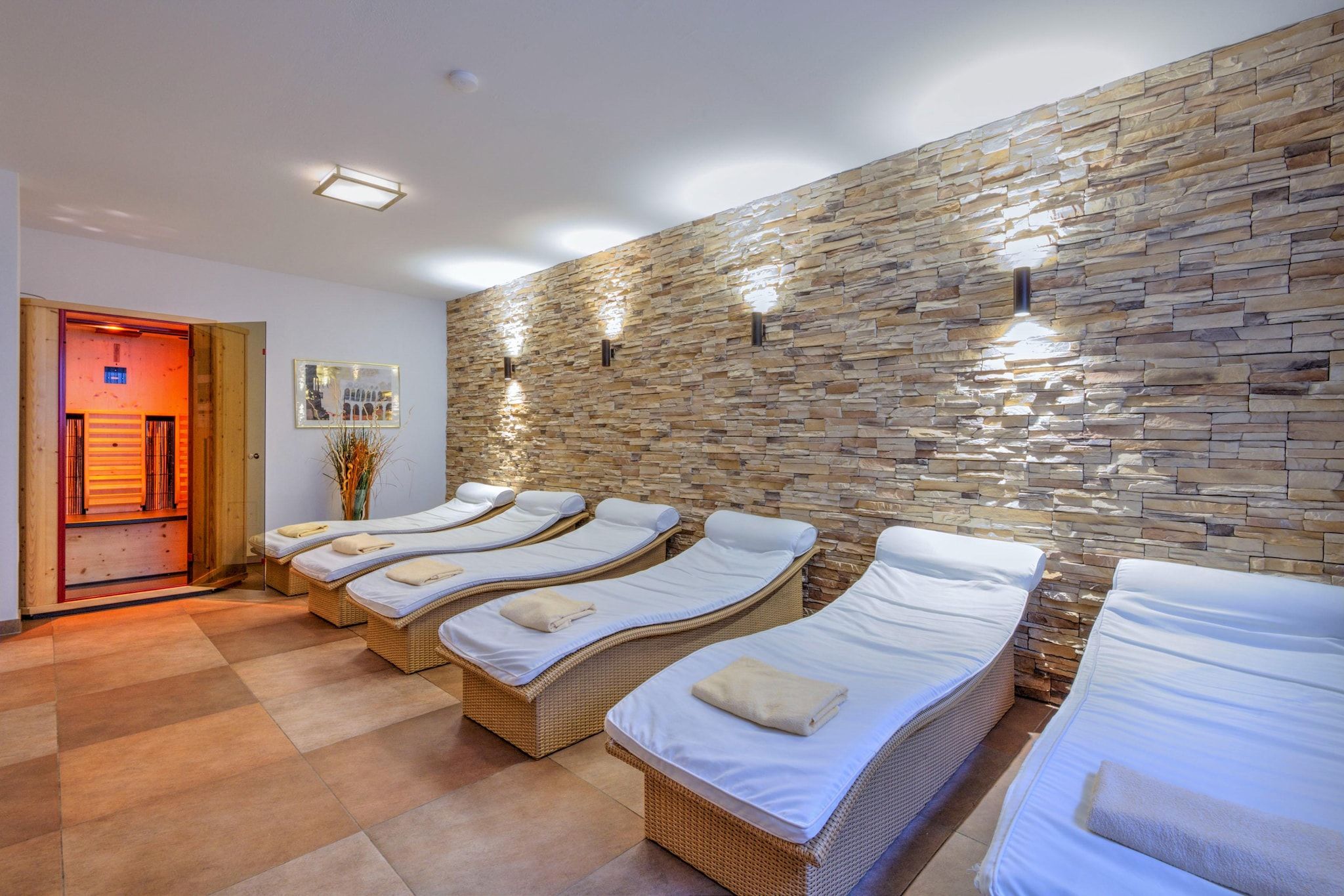 Une salle de spa avec quatre tables de massage alignées contre un mur en pierre, une porte en bois et un tableau encadré accroché au mur.