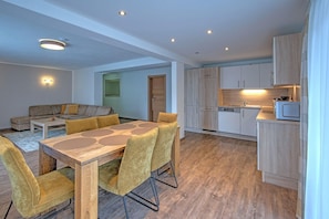 A modern living space with a dining area, sofa, kitchen, and a door leading to another room.