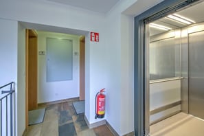 A hallway with a fire extinguisher mounted on the wall, a door labeled '5', and an elevator.