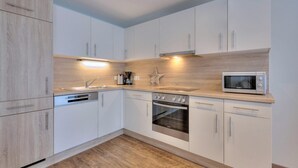 Een moderne keuken met witte kasten, een inbouwoven, een magnetron en een koffiezetapparaat.