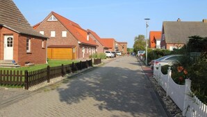 Een woonstraat met bakstenen huizen, een verharde weg en een wit hek.