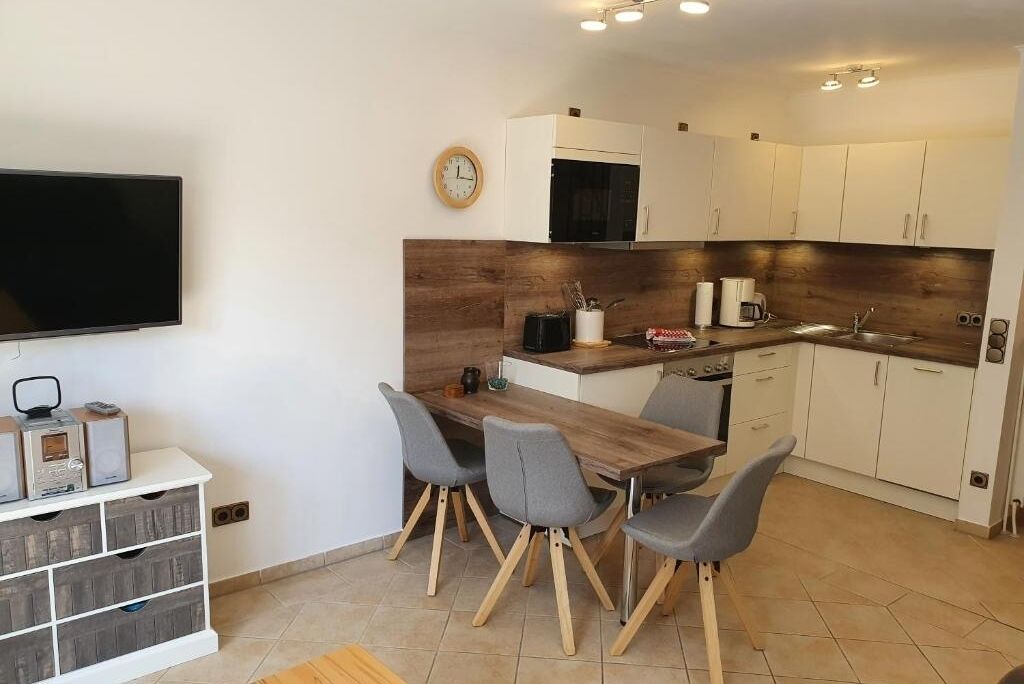 Cozinha moderna com bancada de madeira, armários brancos e área de refeições com mesa de madeira e quatro cadeiras.