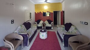 Een kamer met twee tegenover elkaar staande banken, een klein rond tafeltje, een plafondventilator en een aan de muur bevestigde televisie.