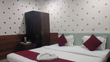 Quarto de hotel com uma cama, duas almofadas, cabeceira, guarda-roupa, mesa de cabeceira com chaleira e parede com padrão geométrico.