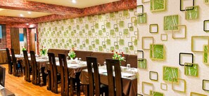 A restaurant interior with brick walls, a patterned wall design, and a long dining table with chairs. - HOTEL MILAND PALACE (Bhubaneshwar)