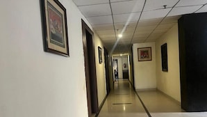 Un long couloir étroit, avec des portes de part et d’autre, menant à différentes pièces. Le couloir est doté d’un sol carrelé et d’un plafond pourvu d’un éclairage encastré.