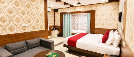 A hotel room with a bed, a sofa, a small table, and a bedside table with a phone.