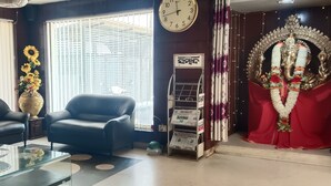 Un salon avec une table basse en verre, deux canapés en cuir noir, un grand vase rempli de tournesols, une horloge et une arche décorative surmontée d’une statue.