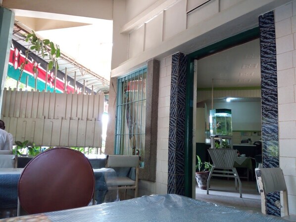 An outdoor seating area with tables and chairs, a covered section with a flag, and a view into a kitchen area.