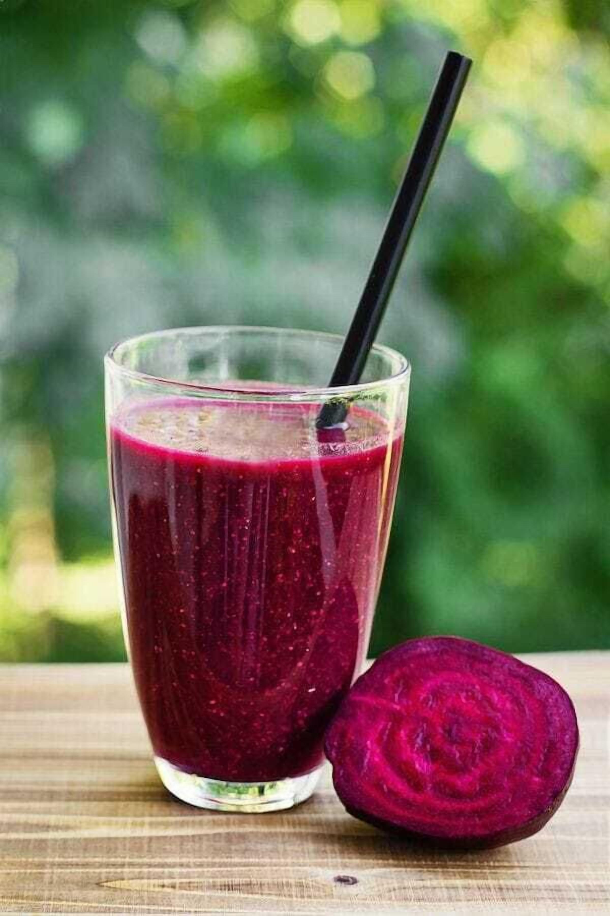 A glass of beetroot juice with a black straw, placed on a wooden surface with a blurred green background.
