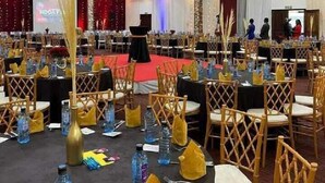 Ein Festsaal mit runden Tischen, goldenen Stühlen und einer Bühne mit rotem Teppich.