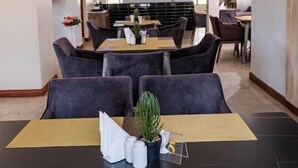 Ein moderner Essbereich mit dunkelgrauen Polsterstühlen, einem zentralen Tisch mit Topfpflanze und einer geometrischen Pendelleuchte.