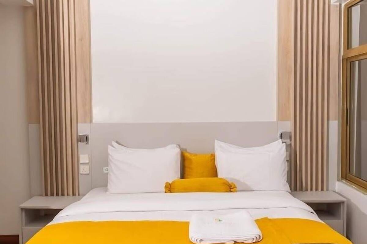 Una habitación de hotel moderna con una cama grande, dos mesitas de noche y un ventanal.