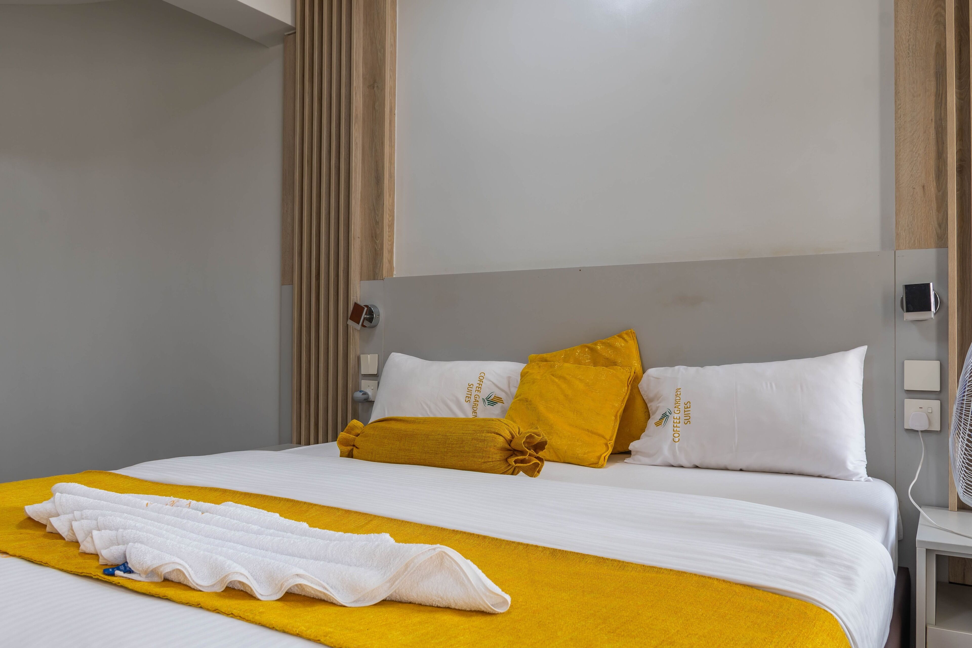 A hotel room with a bed, a bedside table, and a wall-mounted fan.