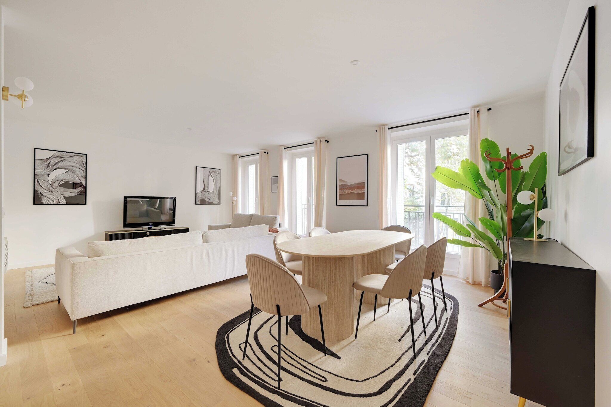 A modern living room with a sofa, dining table, chairs, a TV, and artwork on the walls.
