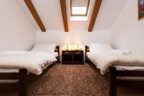 Un dormitorio pequeño y acogedor con dos camas individuales, cabecera de madera, un escritorio pequeño con lámpara y un tragaluz.