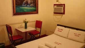 Ein Hotelzimmer mit Bett, Schreibtisch, Stuhl, einem Bild von einem Wasserfall und einer Klimaanlage.