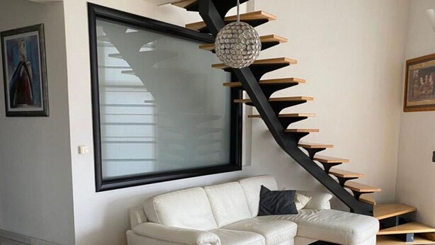 A modern living room with a white leather sofa, a large framed artwork, and a unique black spiral staircase with wooden steps.