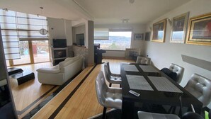 A modern living room with a dining area, large windows, and a fireplace.