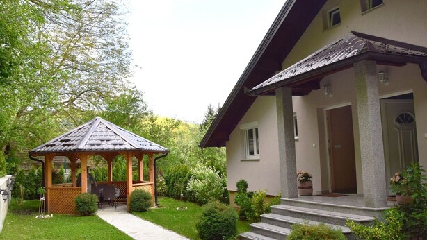 Une maison dotée d’un espace extérieur couvert aménagé en coin salon et d’un chemin pavé menant à l’entrée.
