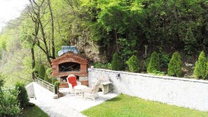 Une cheminée extérieure en briques, avec un mur en pierre, entourée d’une terrasse pavée et de meubles en osier blancs.