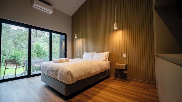 Un dormitorio moderno con una cama grande, una mesita de noche pequeña y vistas al exterior a través de amplios ventanales.