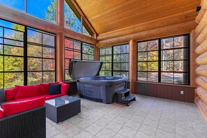 Une cabane en rondins dotée d’un bain à remous, de meubles rouges et noirs et de grandes fenêtres offrant une vue sur le feuillage automnal.