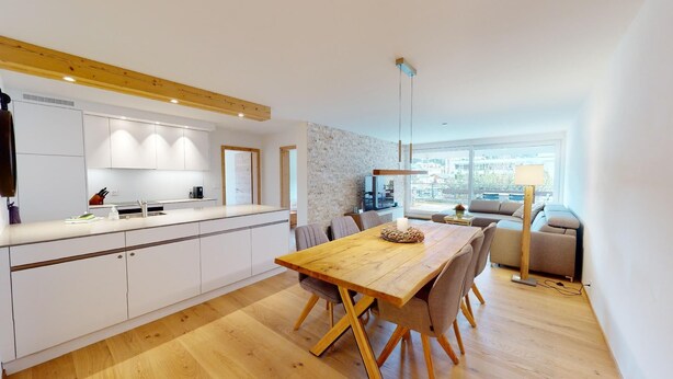 Una cocina moderna con armarios blancos, una mesa de comedor de madera y vistas a la ciudad a través de amplias ventanas.